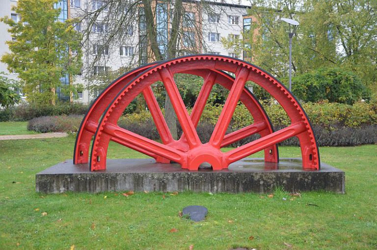 Rotes historisches Rad als Denkmal in einer Grünanlage in Premnitz